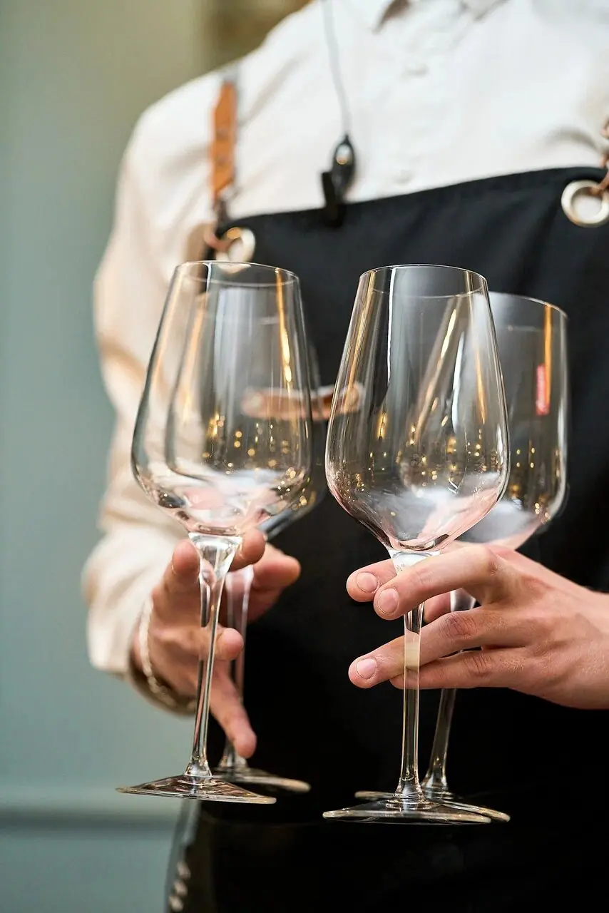 A server's apron with a name badge, holding wine glasses